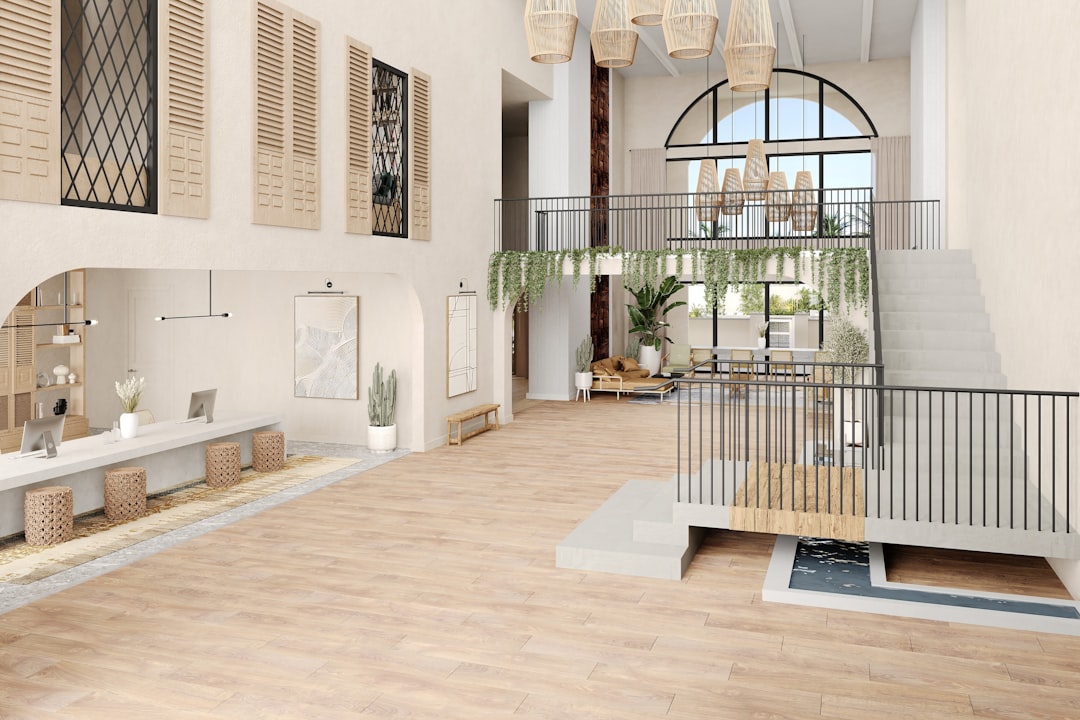 This 3D-rendered image showcases a bright, airy clubroom with modern Mediterranean influences. It features light wood flooring, arched architectural elements, and a soft, neutral palette. The reception area includes woven stools and minimalist counters. A mezzanine with black railings is draped in greenery, and a small water feature flows beneath a bridge, adding a tranquil focal point. Natural textures and lush plants complete the relaxed, upscale atmosphere—ideal for a resort, boutique hotel, or luxury apartment.