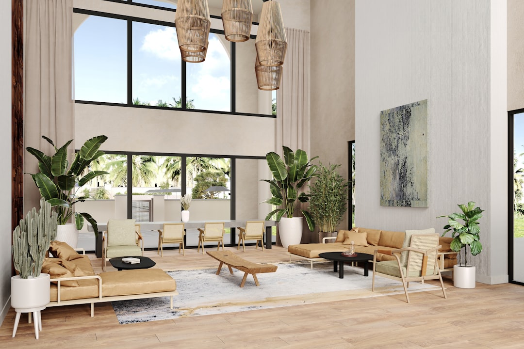 Club curio alt view features a double-height ceiling with an arched window for natural light. Pendant wicker lights hang in a cluster, enhancing the airy, tropical aesthetic. The walls mix textures with wood paneling and a subtle wallpaper finish. Neutral-toned seating includes mid-century modern chairs and contemporary couches paired with woven accents. The light wood flooring complements the abstract area rug. Lush greenery, like banana plants and cacti in white planters, integrates biophilic design. The overall style is modern tropical, with warm tones and natural materials.
