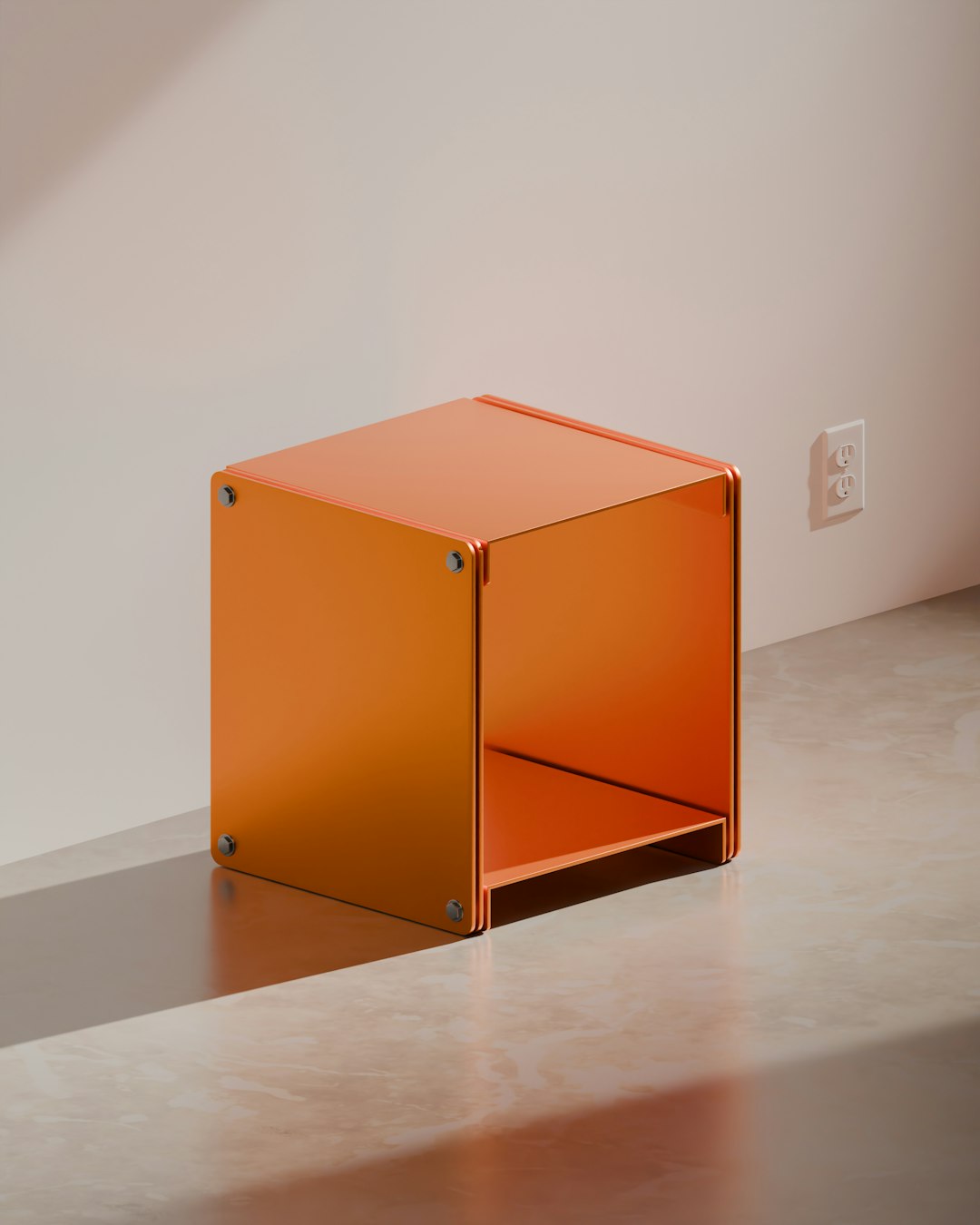 A vibrant orange modular storage cube with industrial-style screw fastenings, sitting on a polished concrete floor next to a light-colored wall with an electrical outlet. The strong shadows highlight its clean, modern design.